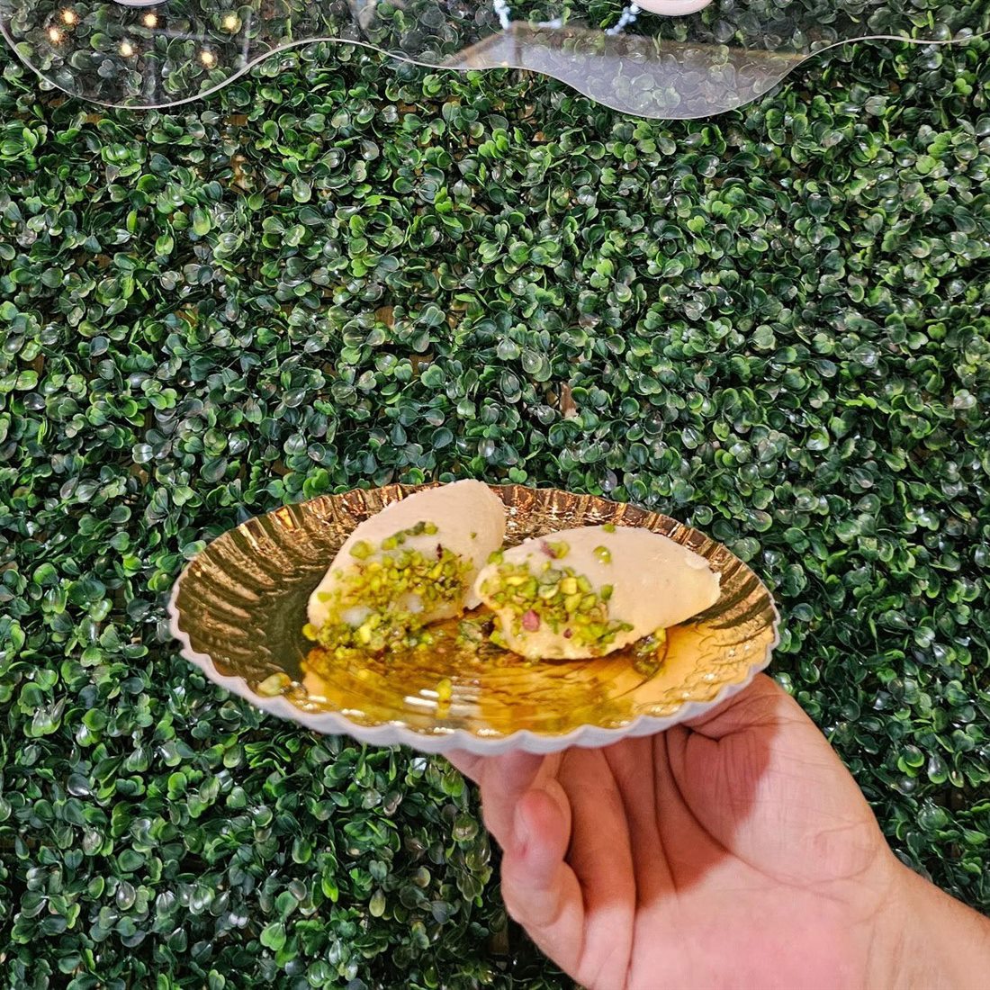 A plate of freshly made kunafa topped with pistachio, held up outside the shop